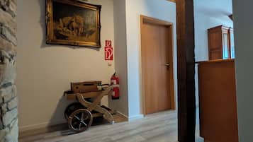 Ein Flur mit einem Holfwagen, einem Feuerlöscher, einer Tür und einem Gemälde an der Wand.