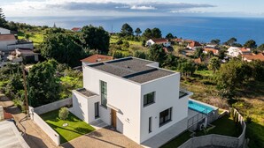 Ein modernes, zweistöckiges Haus mit Pool auf dem Dach, umgeben von üppiger Vegetation und Blick aufs Meer.