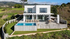 Ein modernes, zweistöckiges Haus mit Swimmingpool, großen Fenstern und Blick auf die umliegende Landschaft.