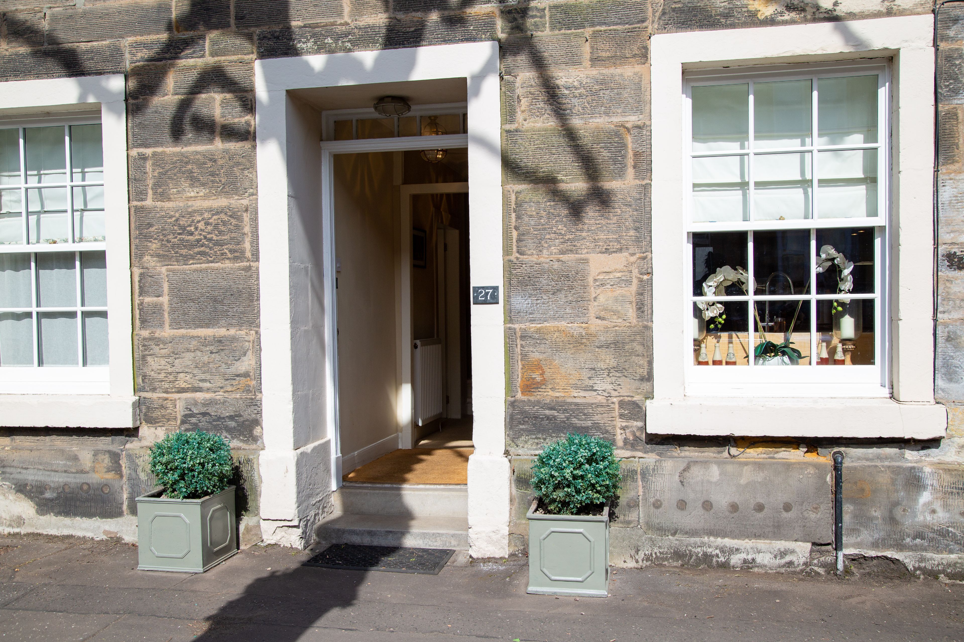 A stone building with a white door, two potted plants, and a sign with the number 27.
