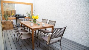 Een houten terras met een tafel, stoelen, een barbecue en een spiegel.