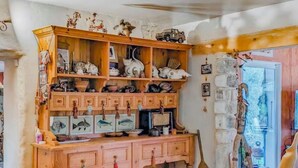 A rustic kitchen with wooden cabinets, shelves with various kitchenware, and a woven rug on the floor.