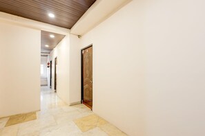 A hallway with a wooden door, white walls, and a tiled floor. - Classic Hotel pix (Jabalpur)