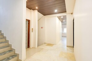 A clean, modern interior with a marble staircase, a wooden ceiling, and a hallway leading to a bright room. - Classic Hotel pix (Jabalpur)