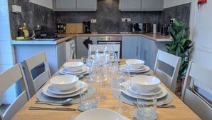 A modern kitchen with grey cabinets, a wooden countertop, and a dining table set for six with white plates, glasses, and cutlery. - Stylish 3BR Home in Swinton - Free Parking (Manchester)