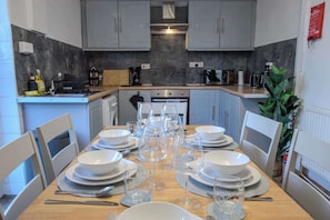 A modern kitchen with grey cabinets, a wooden countertop, and a dining table set for six with white plates, glasses, and cutlery. - Stylish 3BR Home in Swinton - Free Parking (Manchester)