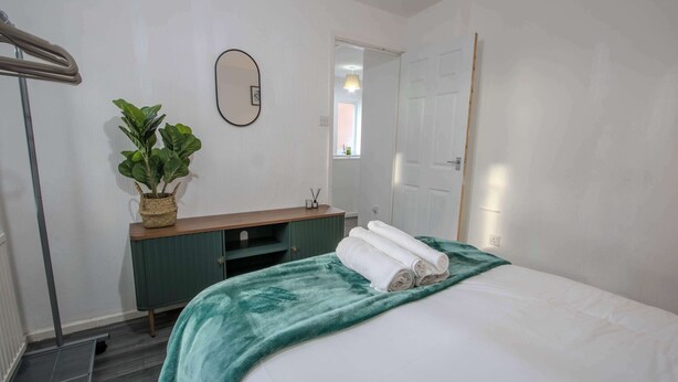 A hotel room with a bed, a bedside table, a mirror, a potted plant, and a door. - Stylish 3BR Home in Swinton - Free Parking (Manchester)