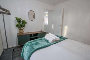 A hotel room with a bed, a bedside table, a mirror, a potted plant, and a door. - Stylish 3BR Home in Swinton - Free Parking (Manchester)