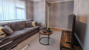 A modern living room with a sofa, a coffee table, a TV, and a door leading to another room. - Stylish 3BR Home in Swinton - Free Parking (Manchester)
