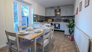 A modern kitchen with grey cabinets, a dining table set for four, and a view through the open door. - Stylish 3BR Home in Swinton - Free Parking (Manchester)