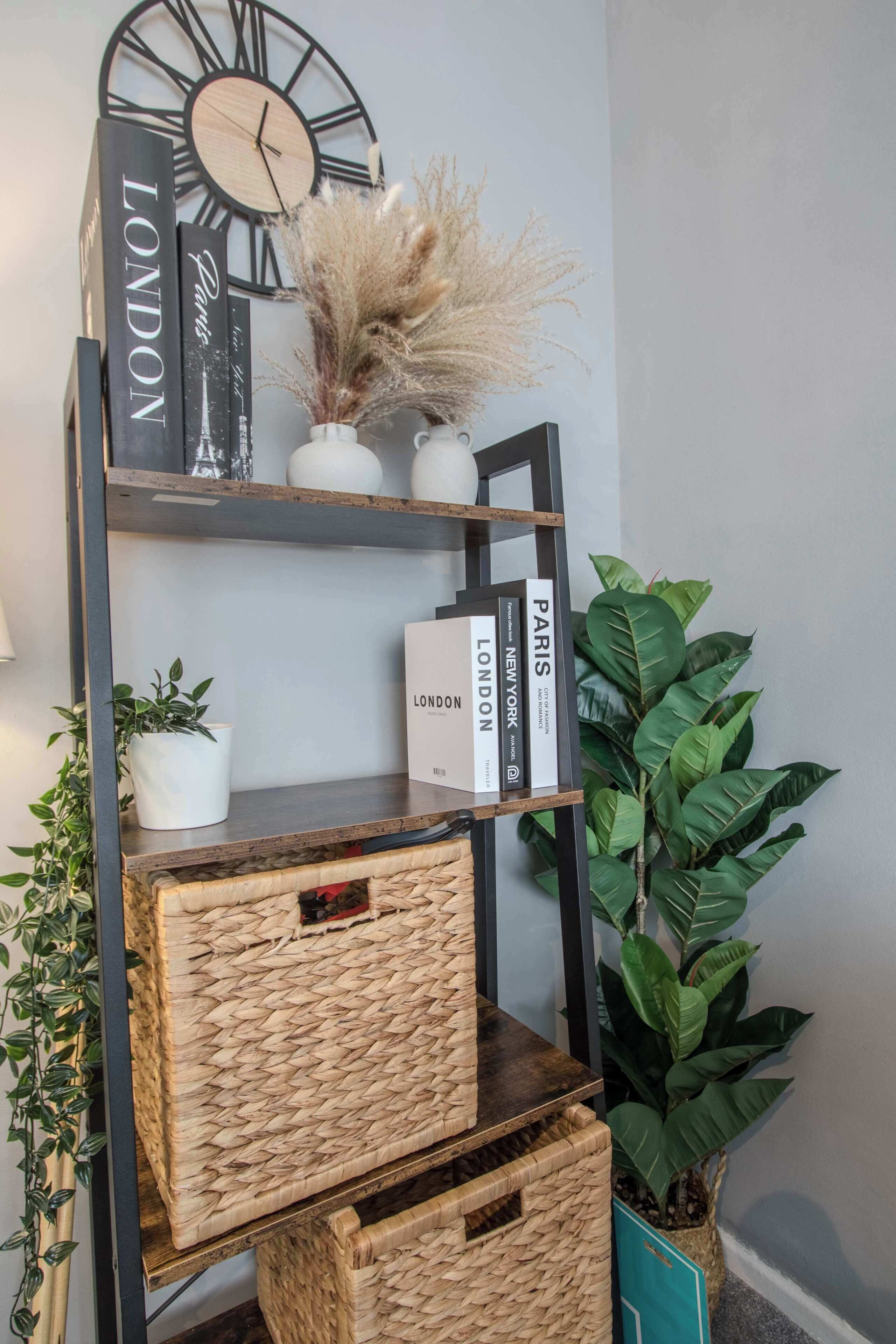 A bookshelf with books and decorative items, including a clock and dried plants.