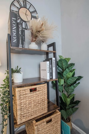 Uma estante com livros e objetos decorativos, incluindo um relógio e plantas secas.