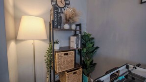 A room with a floor lamp, a wall clock, a bookshelf with books and decorative items, and a small table with a board game. - Stylish 3BR Home in Swinton - Free Parking (Manchester)