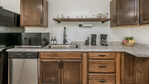 Una cocina con gabinetes de madera, un lavamanos de acero inoxidable, un microondas y una cafetera.