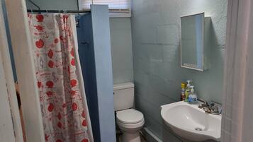 Une salle de bain avec des toilettes blanches, un lavabo avec un miroir et un rideau de douche orné d’un motif sur le thème de la mer.