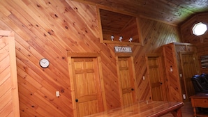 Ein Interieur einer Holzhütte mit einer Holzbank, einem Willkommensschild, einer Uhr und einem Rundfenster.