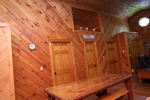 L’intérieur d’un chalet en bois, avec un banc en bois, une pancarte de bienvenue, une horloge et une fenêtre ronde.