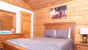 Ein Zimmer mit Holzwänden, einem Bett, einem Nachttisch, einer Lampe und einem Bild an der Wand.
