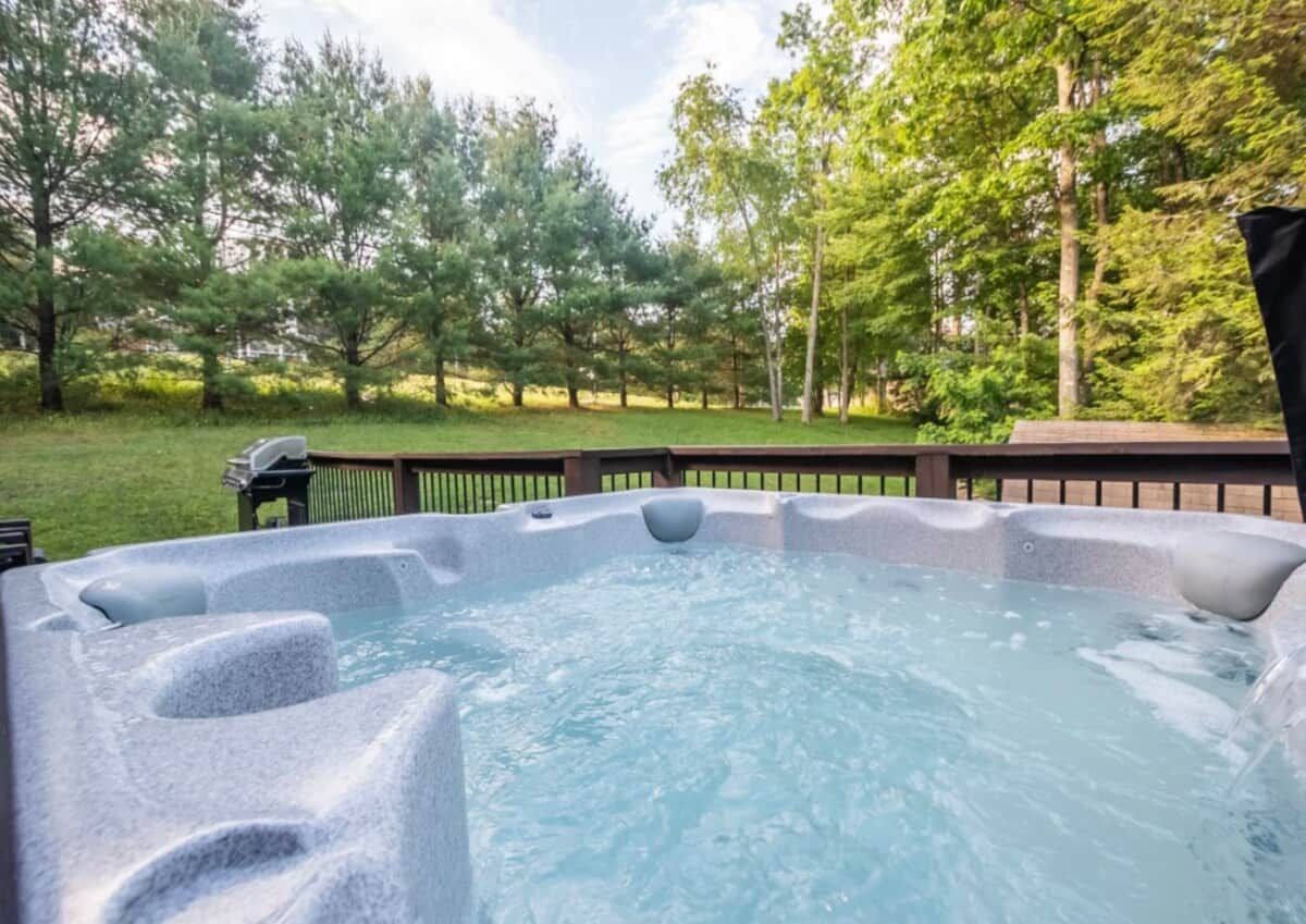 A hot tub in a backyard with a wooden deck and trees in the background.