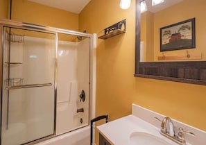 Ein Badezimmer mit einer gläsernen Duschkabine, einem weißen Waschbecken und einem gerahmten Bild an der Wand.