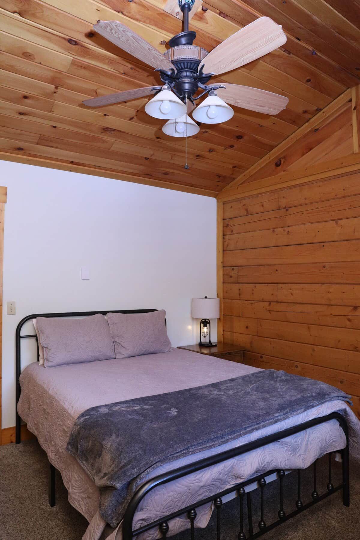 A bedroom with a bed, a nightstand, a lamp, and a ceiling fan.