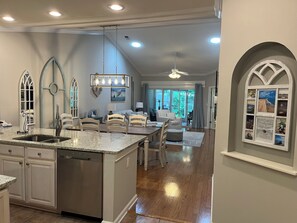 A spacious kitchen with a central island, a dining area with a chandelier, and a view into the living room. - Beautiful True Blue 3 Bedroom 2 Bathroom Garden Home (Pawleys Island)