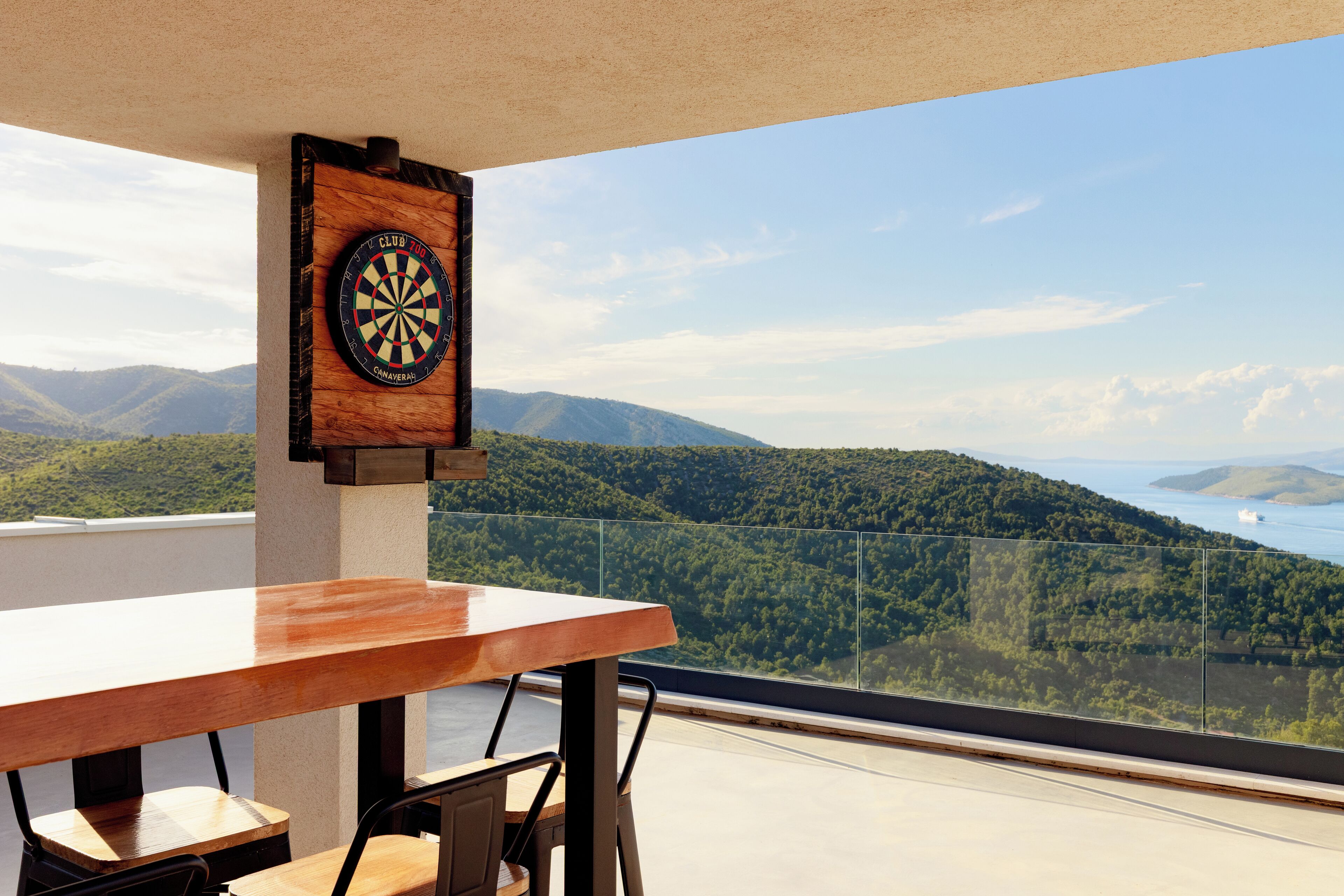 A table with chairs, a dartboard, and a scenic mountain view.