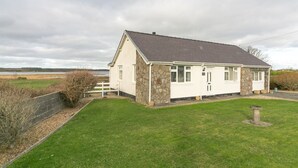 A white cottage with stone walls and a sloped roof, situated in a grassy area with a view of a lake.