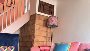 Un soggiorno con una poltrona blu, un divano rosa, una parete in pietra e una scala in legno.