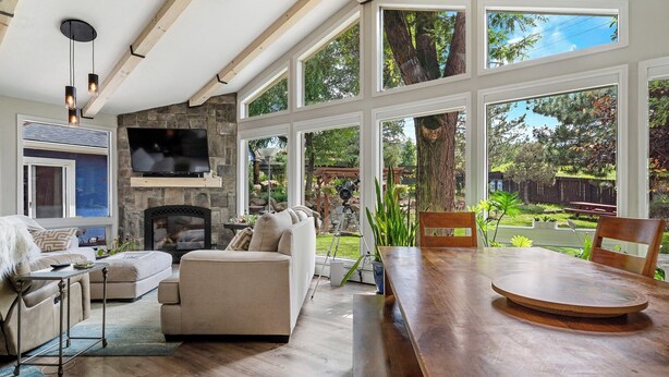 A spacious living room with a stone fireplace, large windows, and a wooden dining table. - Broadmoor Spacious 4-bd 3 bth house with Mountain View’s 3 mins to The Broadmoor (Colorado Springs)