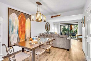 Una sala de estar moderna con comedor, un cuadro abstracto grande, una araña y un cartel que indica la dirección a la playa.