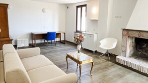 Ein Wohnzimmer mit einer Couch, einem Couchtisch mit Blumen, einem Kamin, einem Schreibtisch mit Stuhl und einem Fenster.