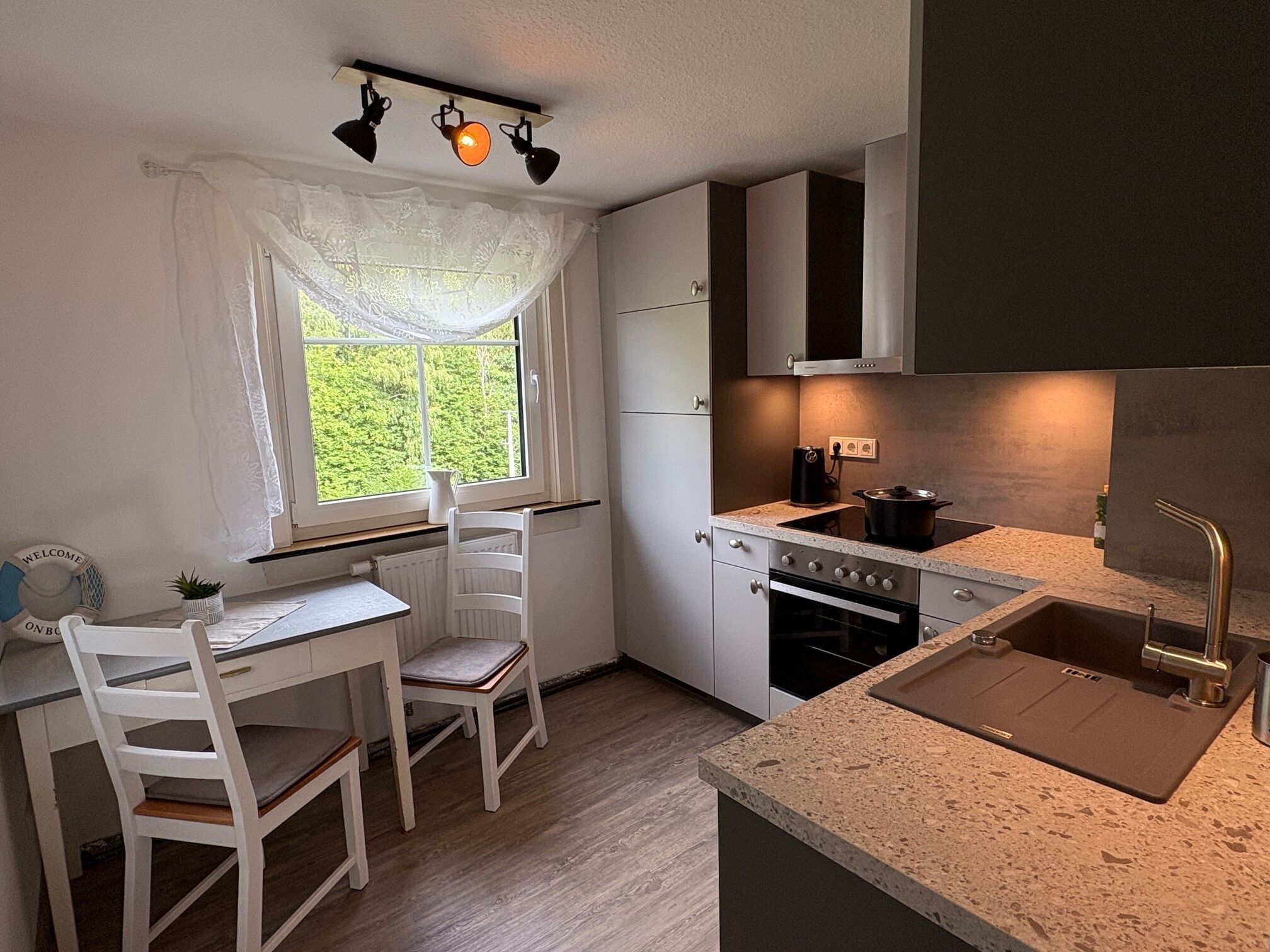 Une cuisine compacte dotée d’une fenêtre, d’un évier, d’une cuisinière et d’un coin repas avec des chaises.