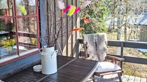 A wooden deck with a table and chairs, a white vase with branches, and a window with red trim. - Gördalen by Interhome (Särna)