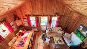 A cozy cabin with a wooden interior, a dining area with a table and chairs, a sofa, and a window with red curtains. - Gördalen by Interhome (Särna)