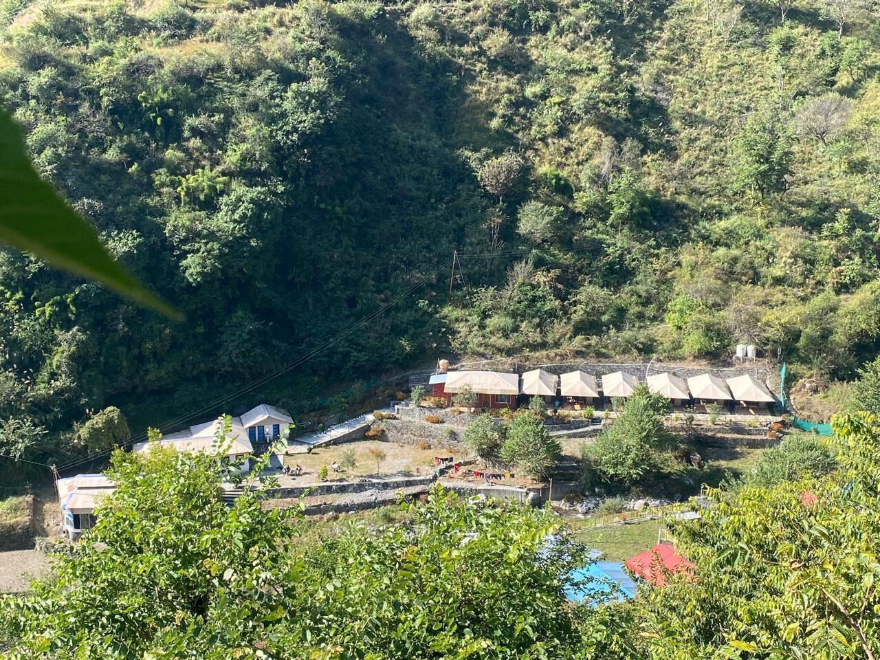 A hillside with several small buildings, likely a guesthouse or lodge, with a few tents and a few people visible.