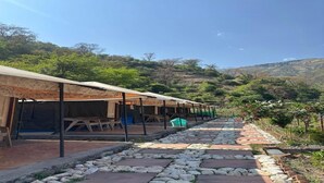 A row of simple, open-air structures with tables and chairs, set against a hilly backdrop. - Aquatic resort (Chakrata)