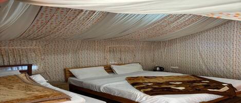 Una habitación con dos camas de madera, ropa de cama blanca y una cama con dosel y dosel estampado.