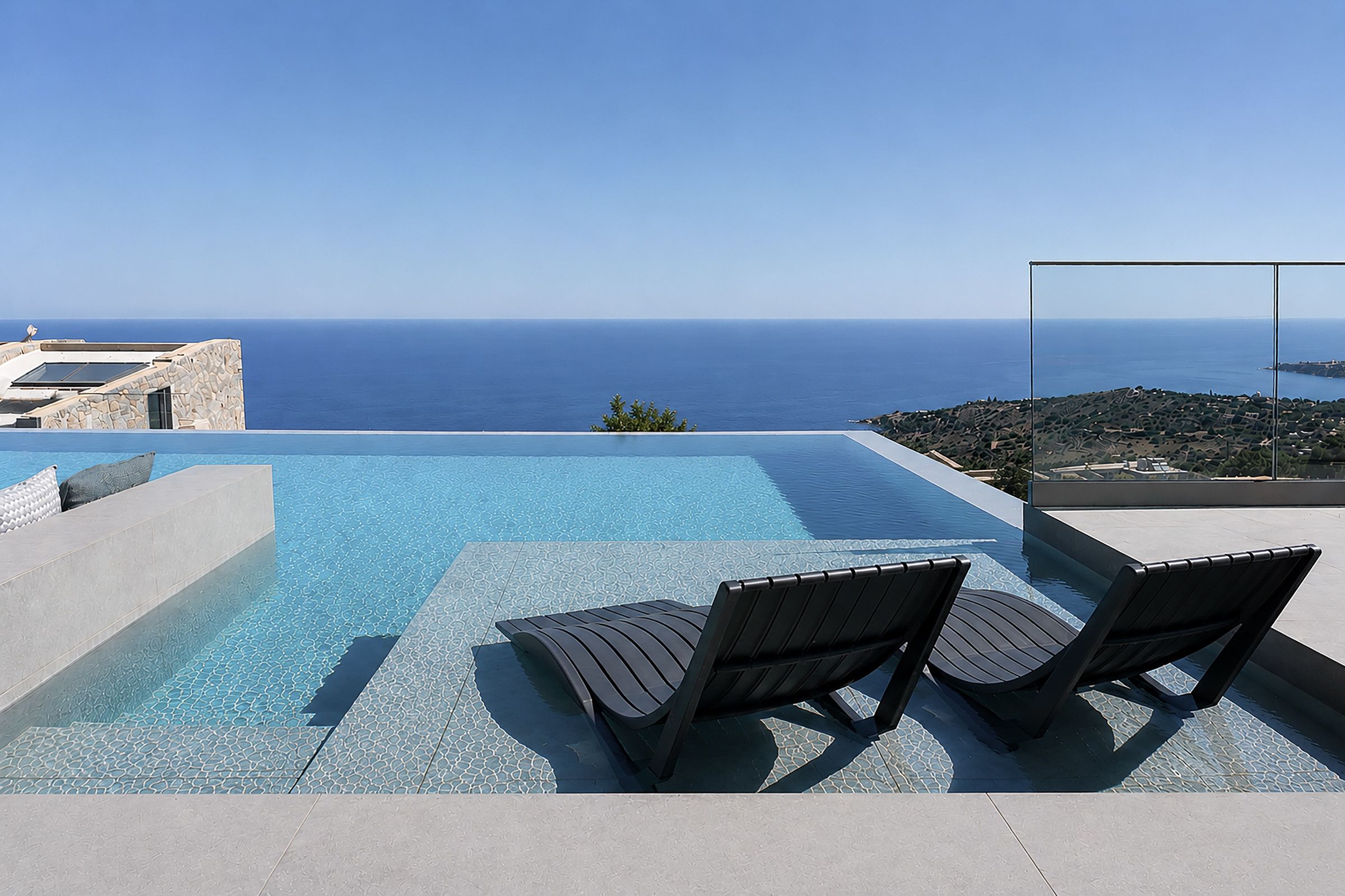 A swimming pool with two lounge chairs and a view of the sea.