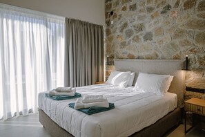 Ein modernes Hotelzimmer mit einer Wand aus Steinimitat, einem großen Bett mit weißer Bettwäsche und Blick durch transparente Vorhänge.