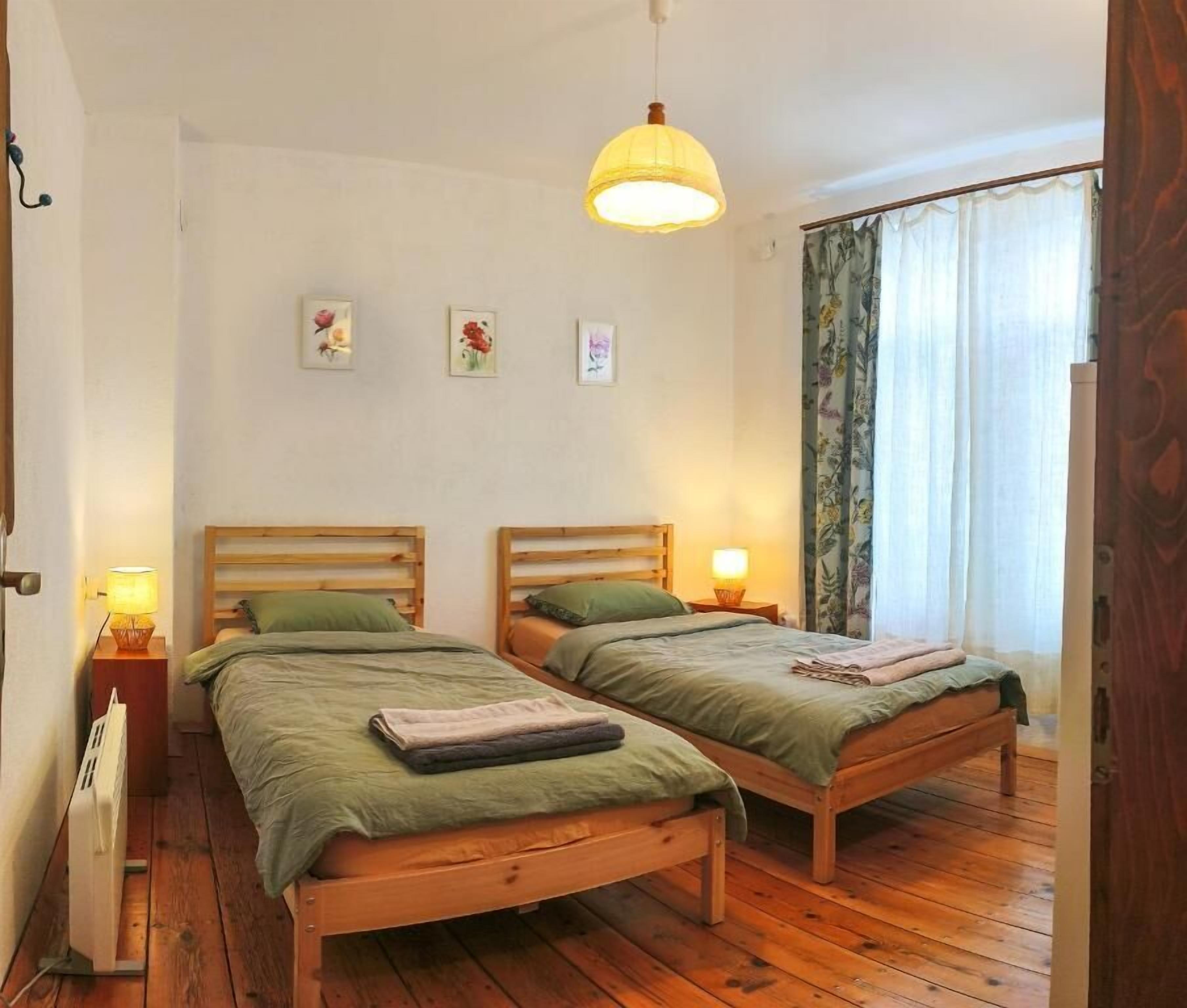 A room with two wooden beds, a hanging lamp, and a window with curtains.