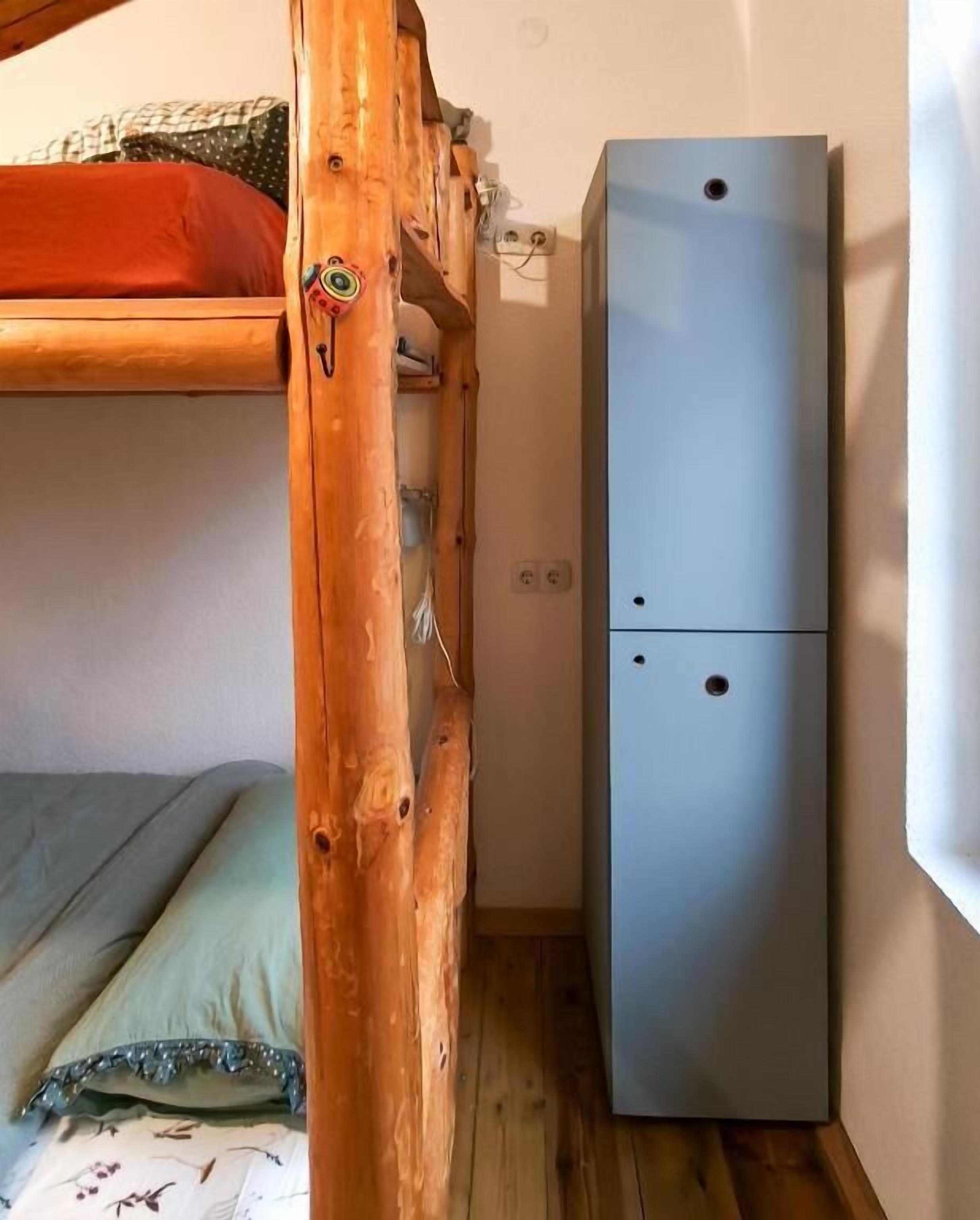 A bunk bed with a wooden headboard, a small cabinet, and a wall socket.
