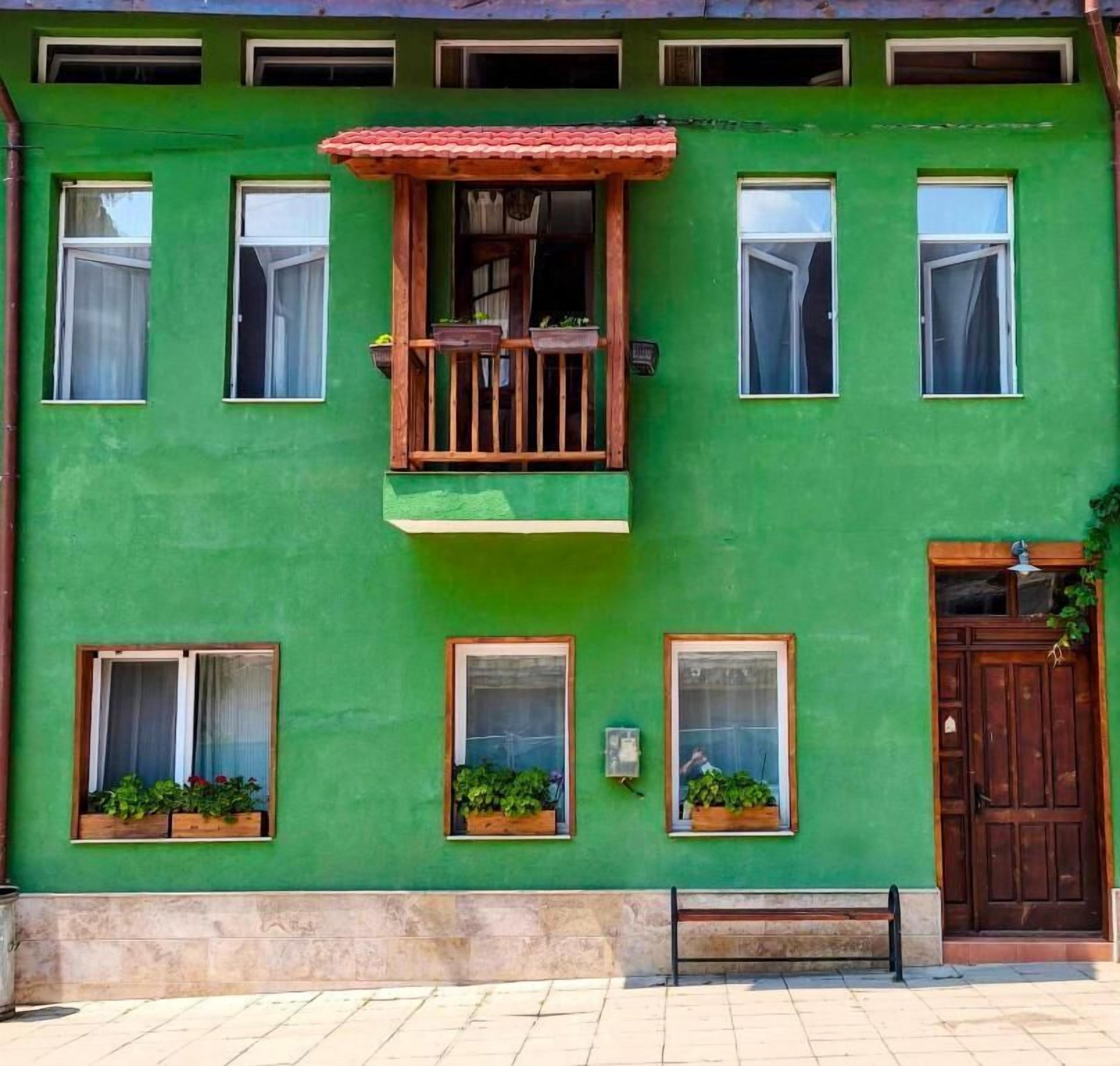Ein grünes Gebäude mit Holzbalkon, zahlreichen Fenstern und einer Tür.