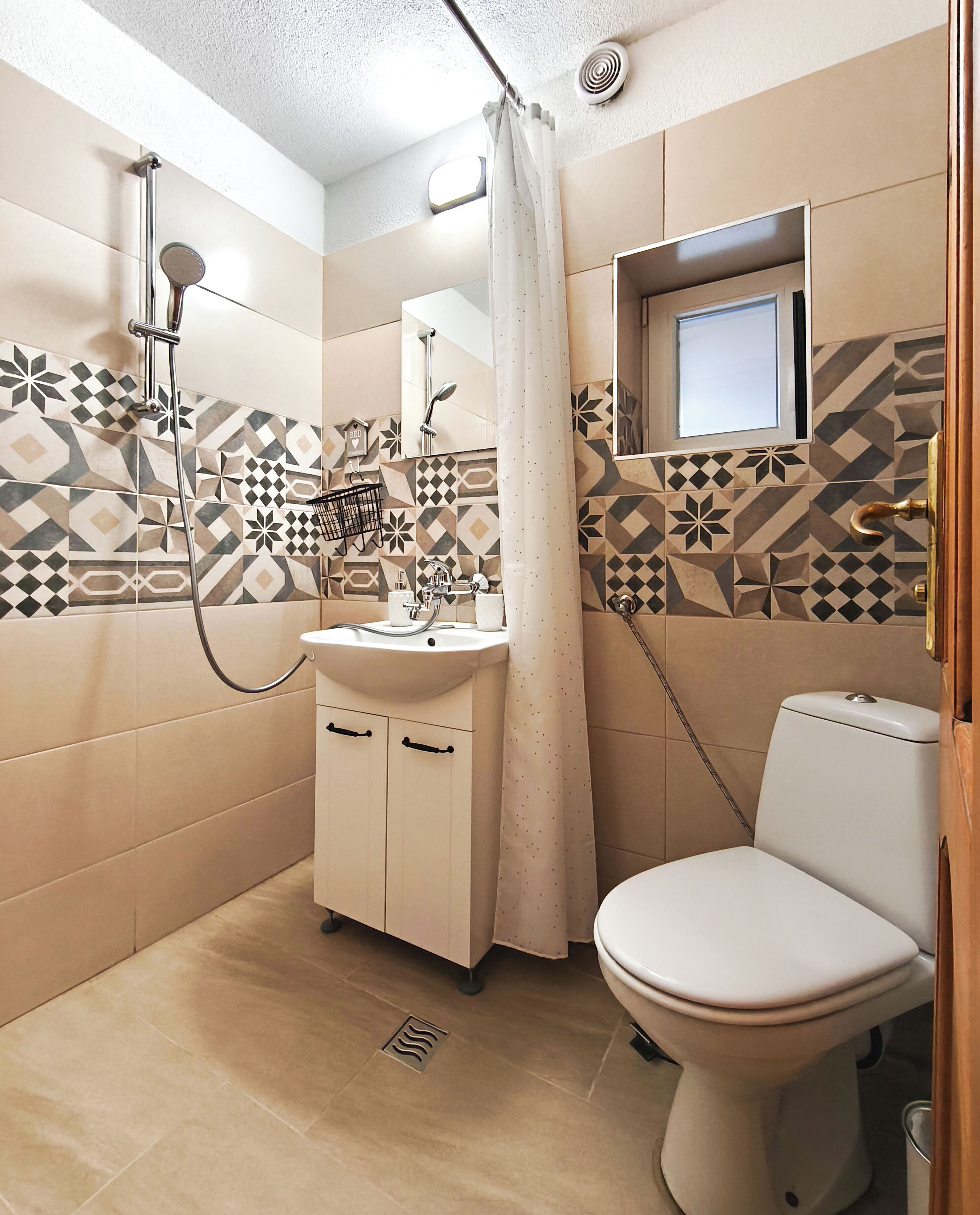 Un baño con ducha, inodoro y lavamanos, con azulejos estampados y una ventana.