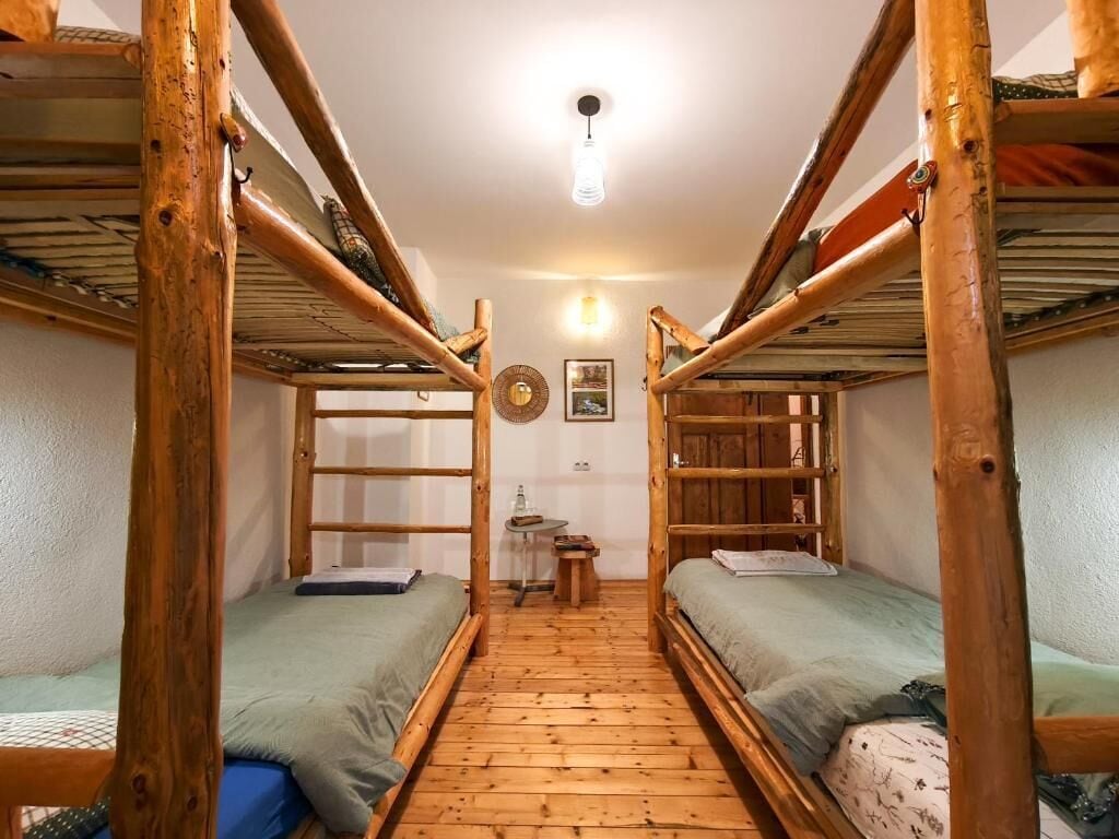 Quarto com beliches de madeira, uma pequena mesa e um relógio de parede.