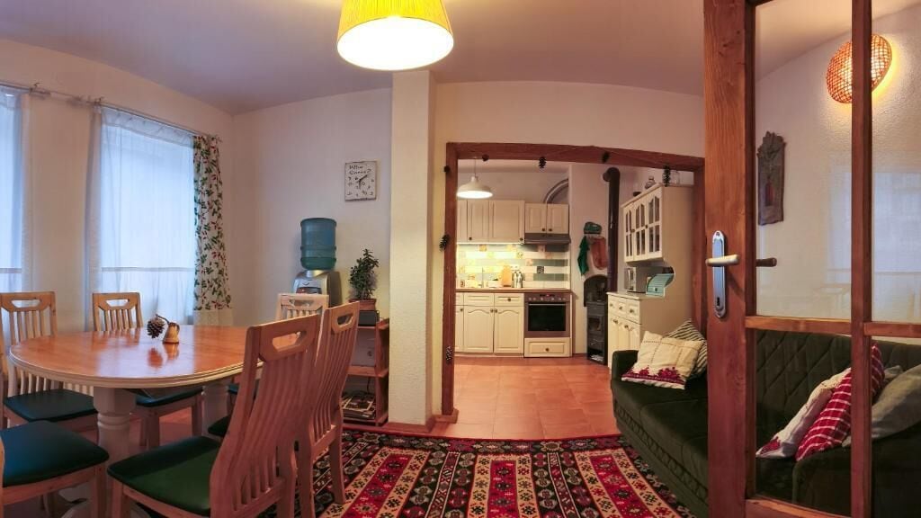A cozy living room with a dining table, chairs, a sofa, and a kitchen in the background.