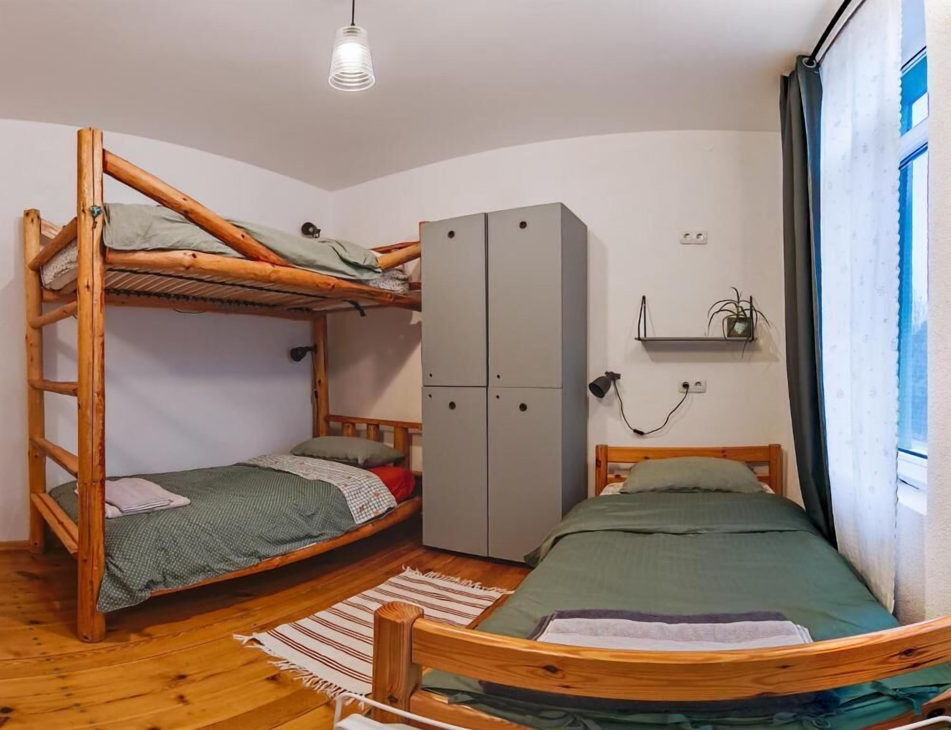 Habitación con literas, un armario, una pequeña estantería y una lámpara colgante.