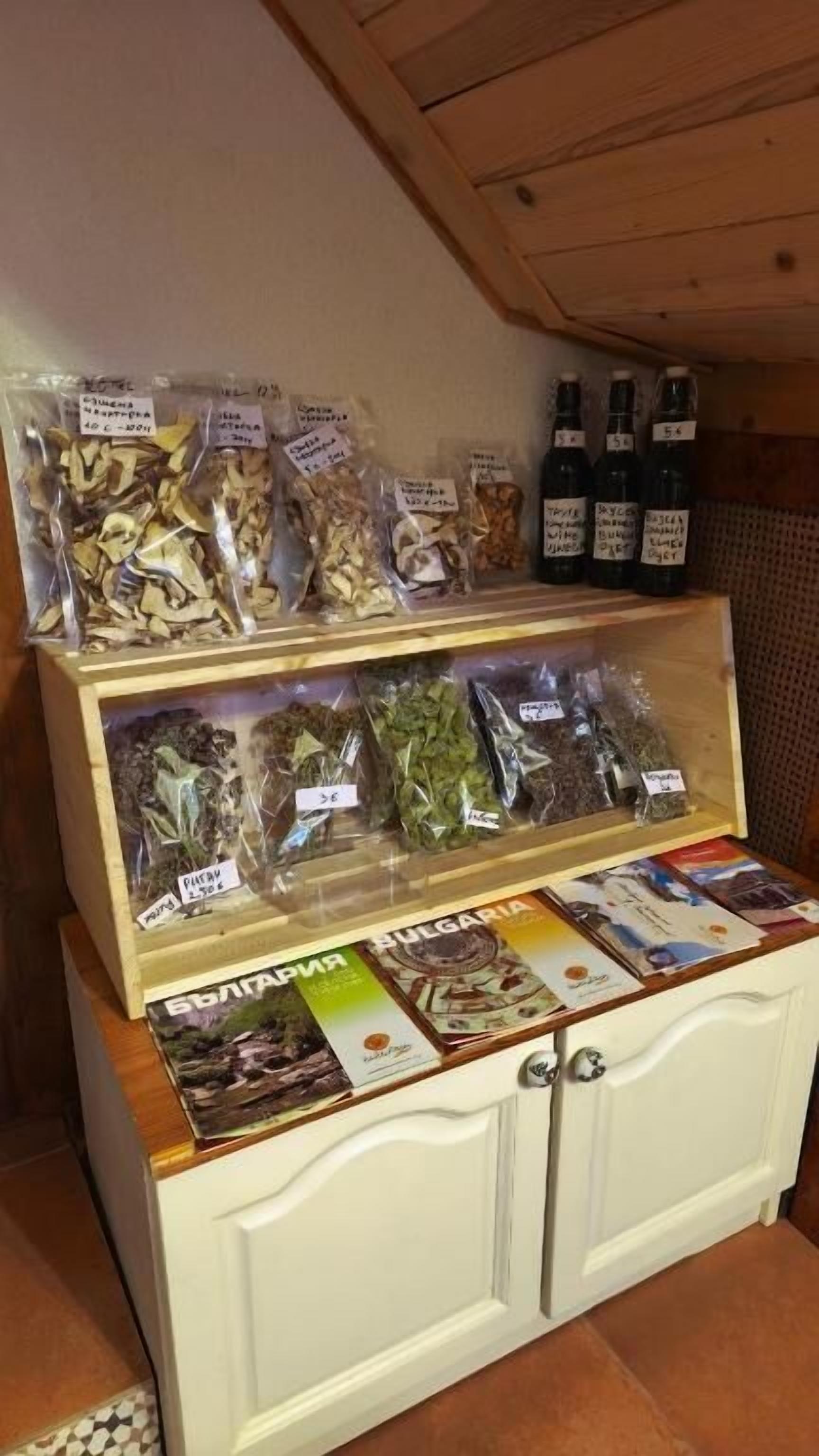 Un meuble en bois doté de portes en verre, renfermant des herbes et des épices séchées, et une étagère au-dessus, où sont disposées des bouteilles et une brochure.