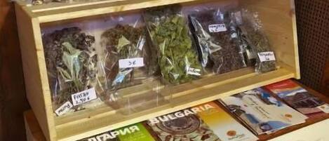 Un meuble en bois doté de portes en verre, renfermant des herbes et des épices séchées, et une étagère au-dessus, où sont disposées des bouteilles et une brochure.