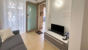 A modern living room with a sofa, a flat-screen TV, and a glass door leading to a balcony.